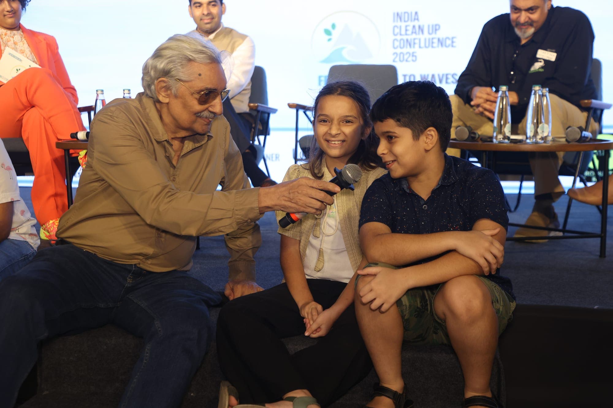 An older delegate passing a microphone to a young boy seated beside him during a session