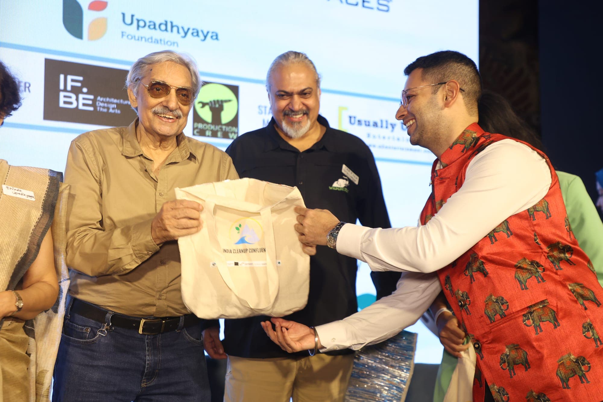 Two delegates exchanging an ICUC tote bag in front of the sponsor backdrop