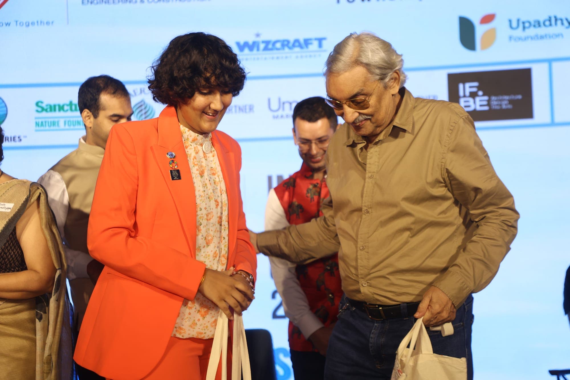 Two delegates shaking hands over an ICUC tote bag in front of the sponsor backdrop