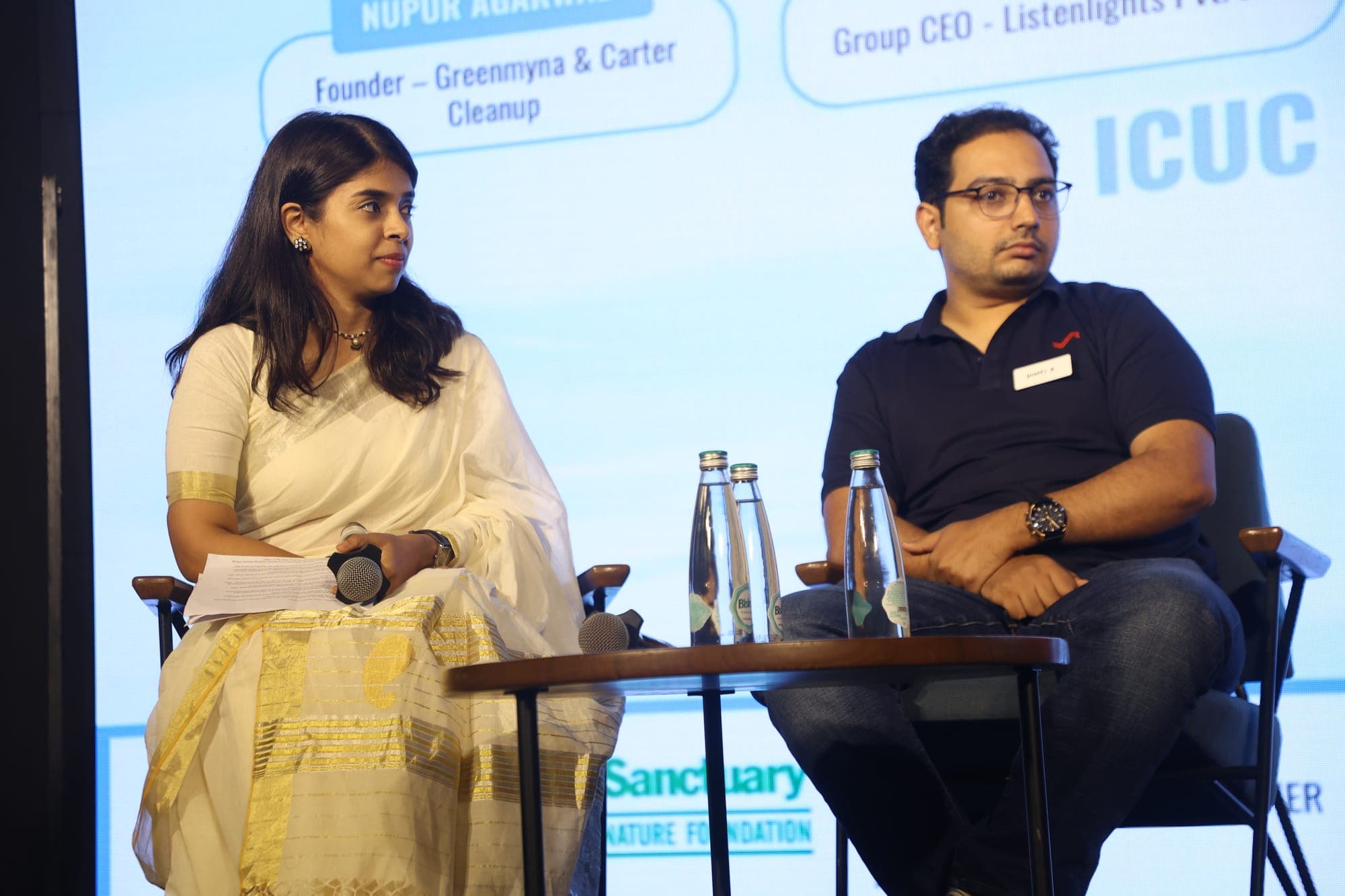 Two panellists seated in conversation on stage under the ICUC screen