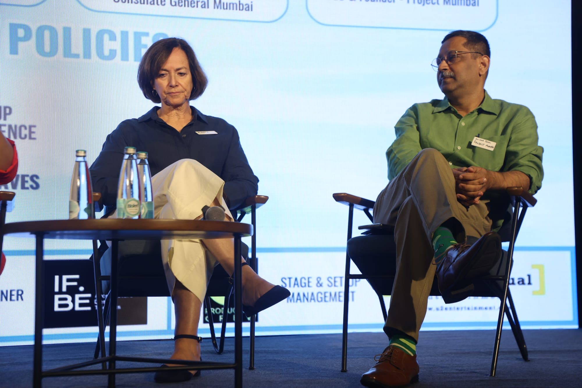 Two panellists mid-discussion on stage in front of the From Ripples to Waves backdrop
